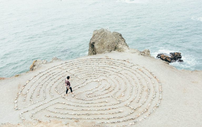 Einzelcoaching-Persönlichkeitsentwicklung-Perspektive Eine Person geht durch ein steinernes Labyrinth am Meer und sucht nach Orientierung.